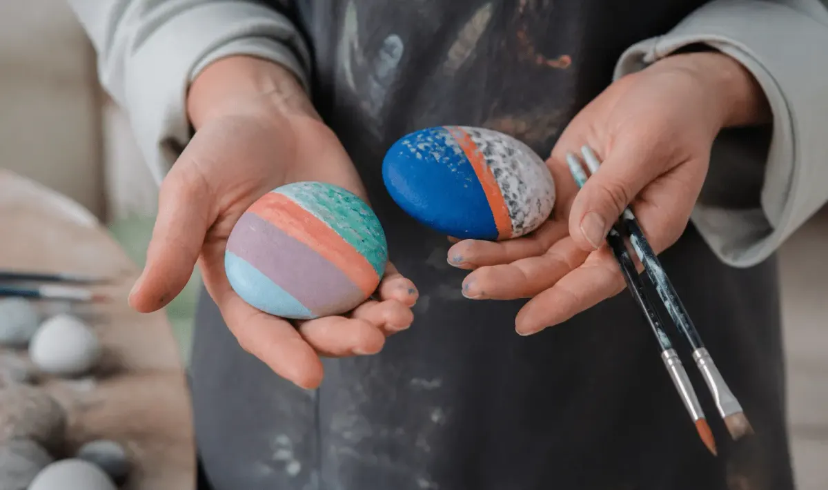Mains tenant des galets plats colores avec pinceaux et peinture