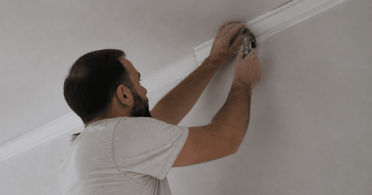 Ouvrier installant moulure decorative blanche au plafond avec outil