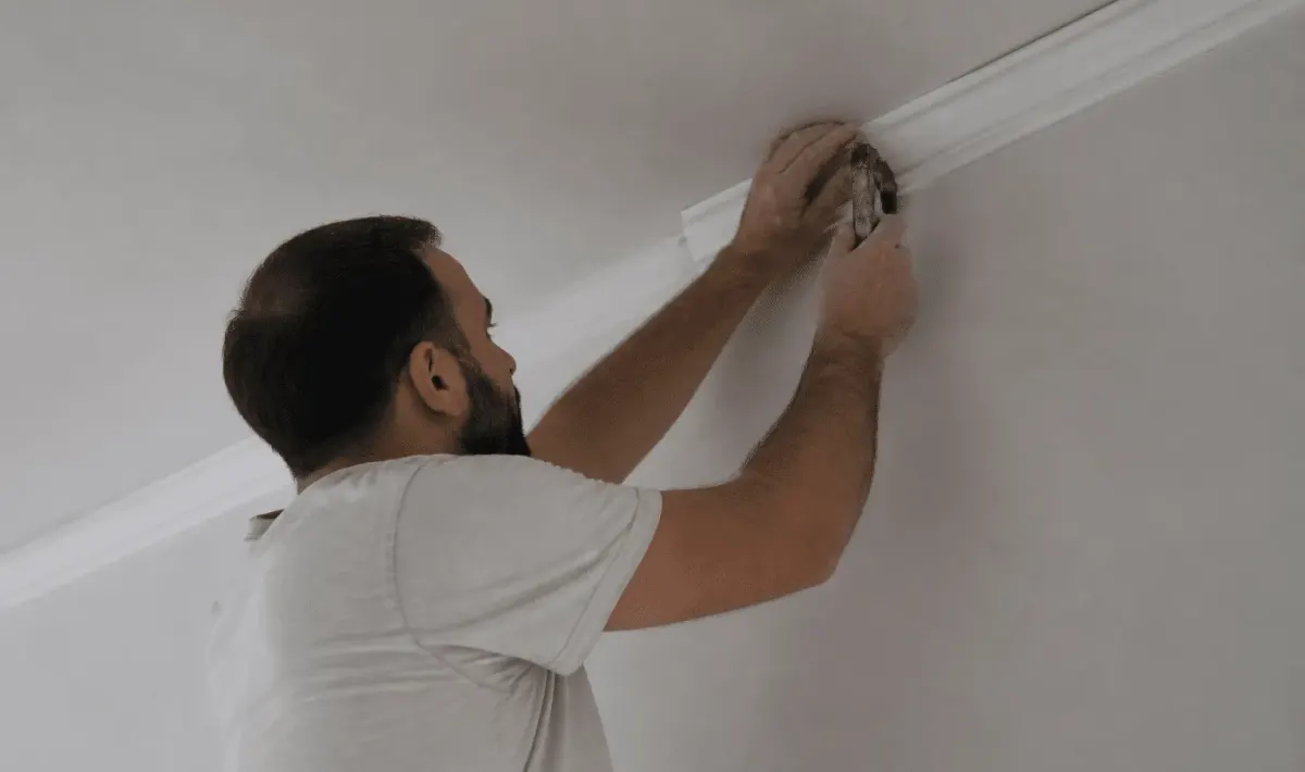 Ouvrier installant moulure decorative blanche au plafond avec outil