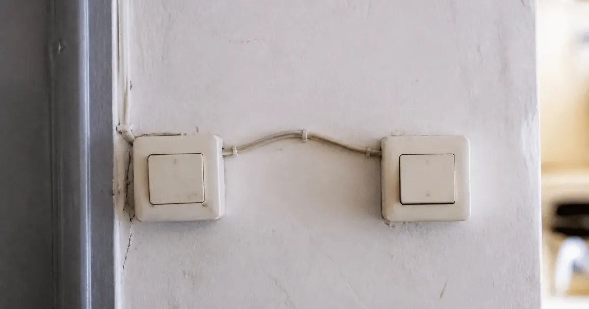 Deux interrupteurs muraux blancs connectes par fils electriques visibles