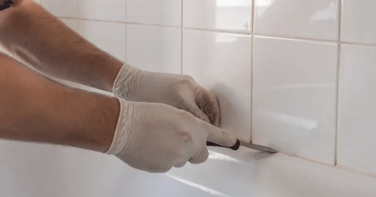Mains gantees grattant joint carrelage blanc salle bain