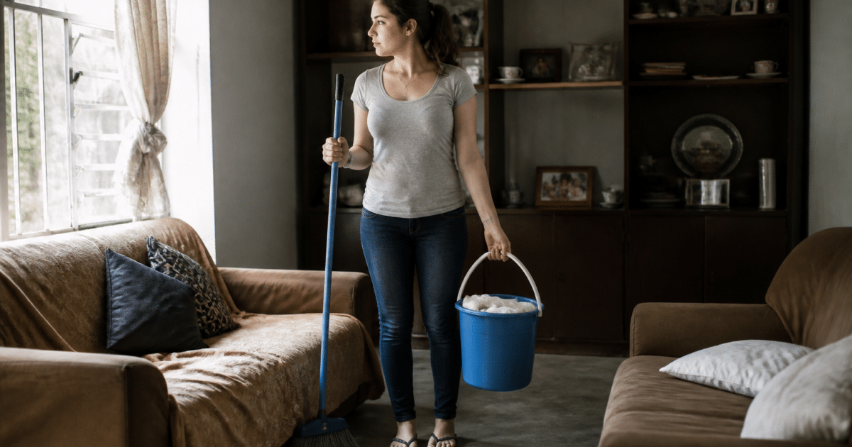 Personne tenant balai et seau rempli debout dans salon