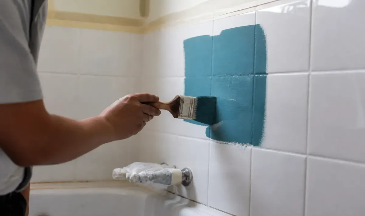 pinceau appliquant peinture coloree sur carreaux blancs salle bain