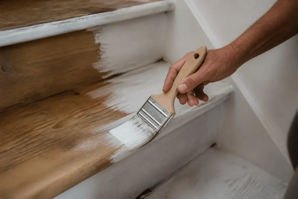Pinceau appliquant peinture blanche sur marches escalier bois