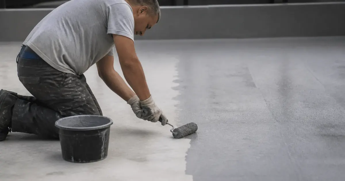Ouvrier appliquant peinture grise sur dalle beton horizontale