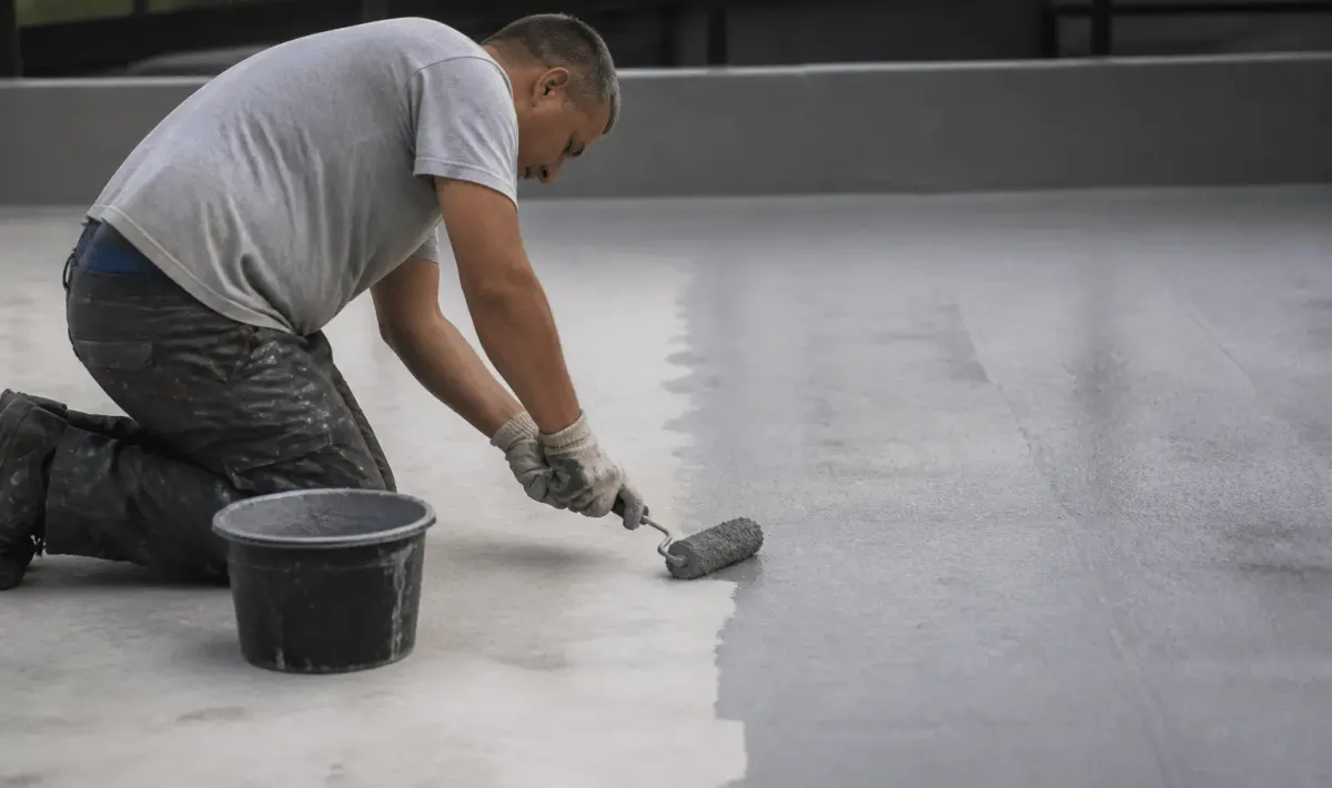 Ouvrier appliquant peinture grise sur dalle beton horizontale