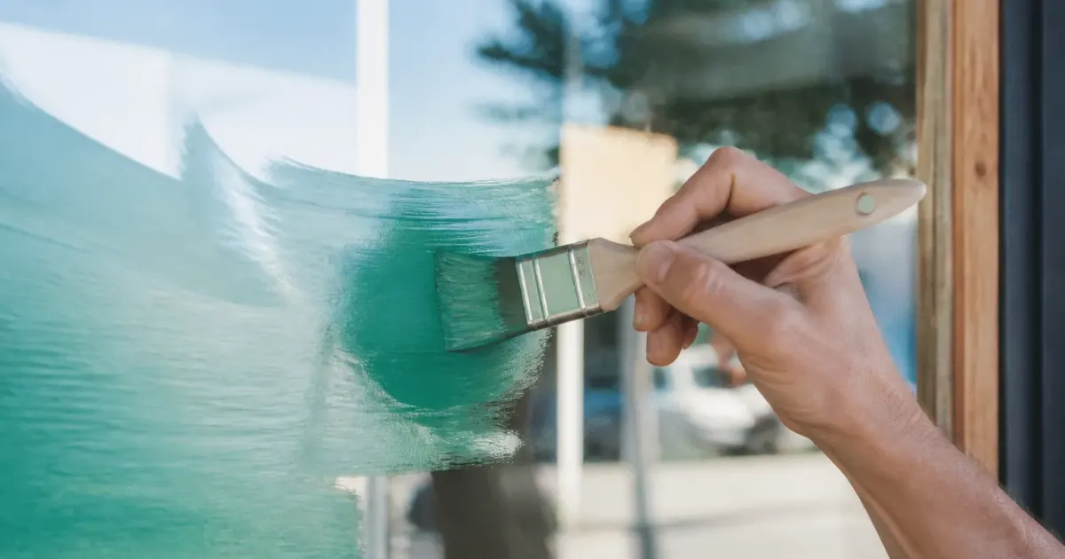 Pinceau appliquant peinture coloree sur surface vitree transparente