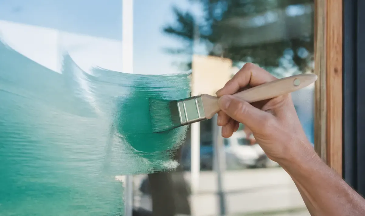 Pinceau appliquant peinture coloree sur surface vitree transparente