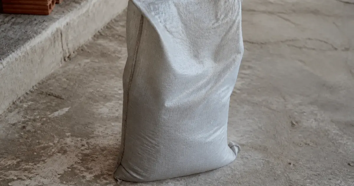 Sac de ciment gris posé debout sur sol beton