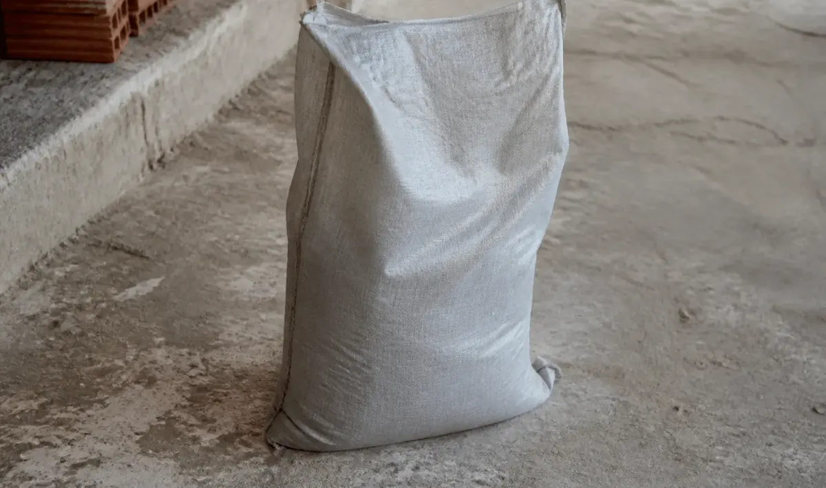 Sac de ciment gris posé debout sur sol beton