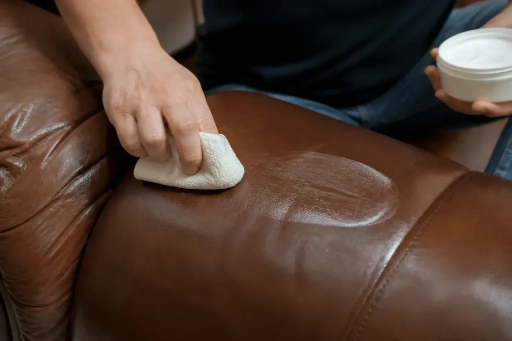 Main appliquant produit nourrissant sur cuir marron