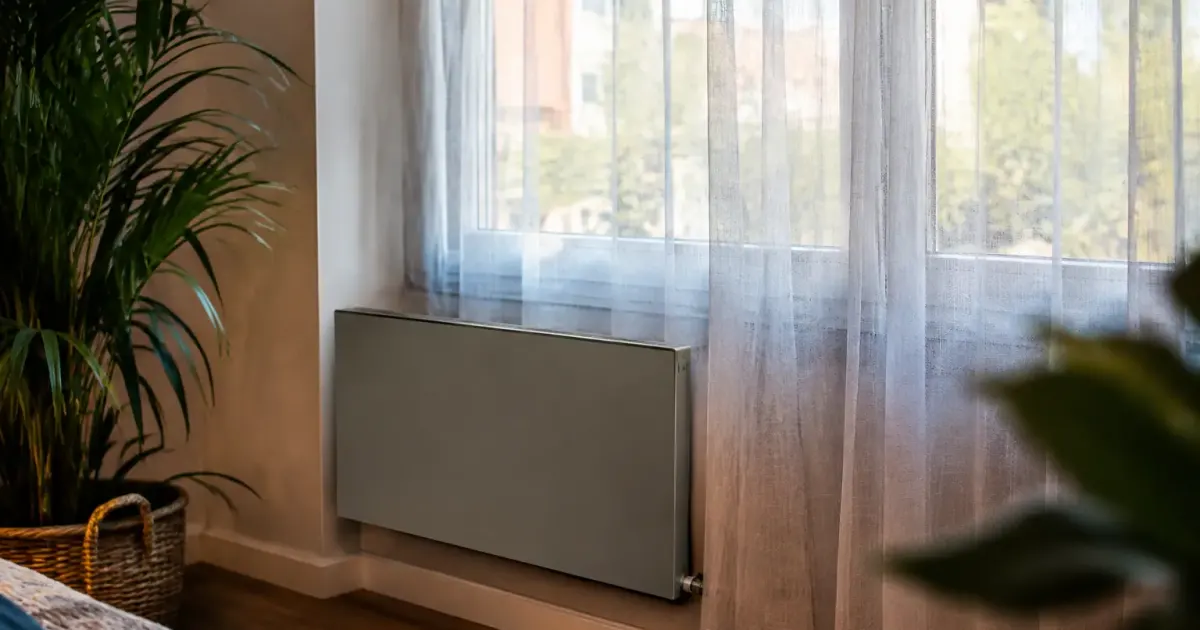 Convecteur gris fixe au mur, voilage terne devant fenetre