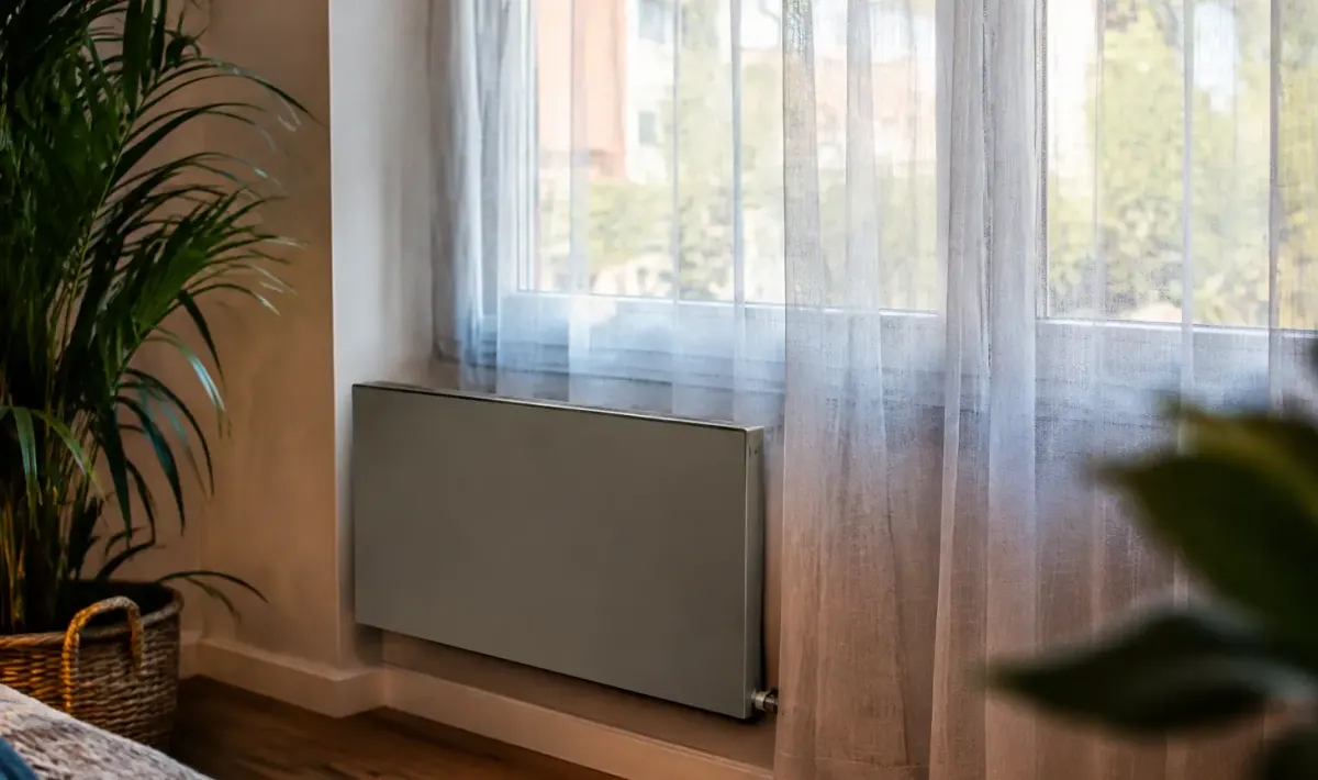 Convecteur gris fixe au mur, voilage terne devant fenetre
