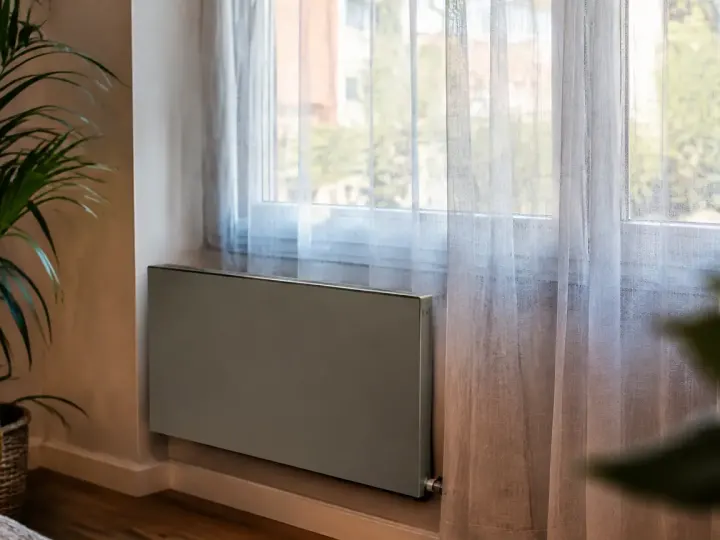 Convecteur gris fixe au mur, voilage terne devant fenetre