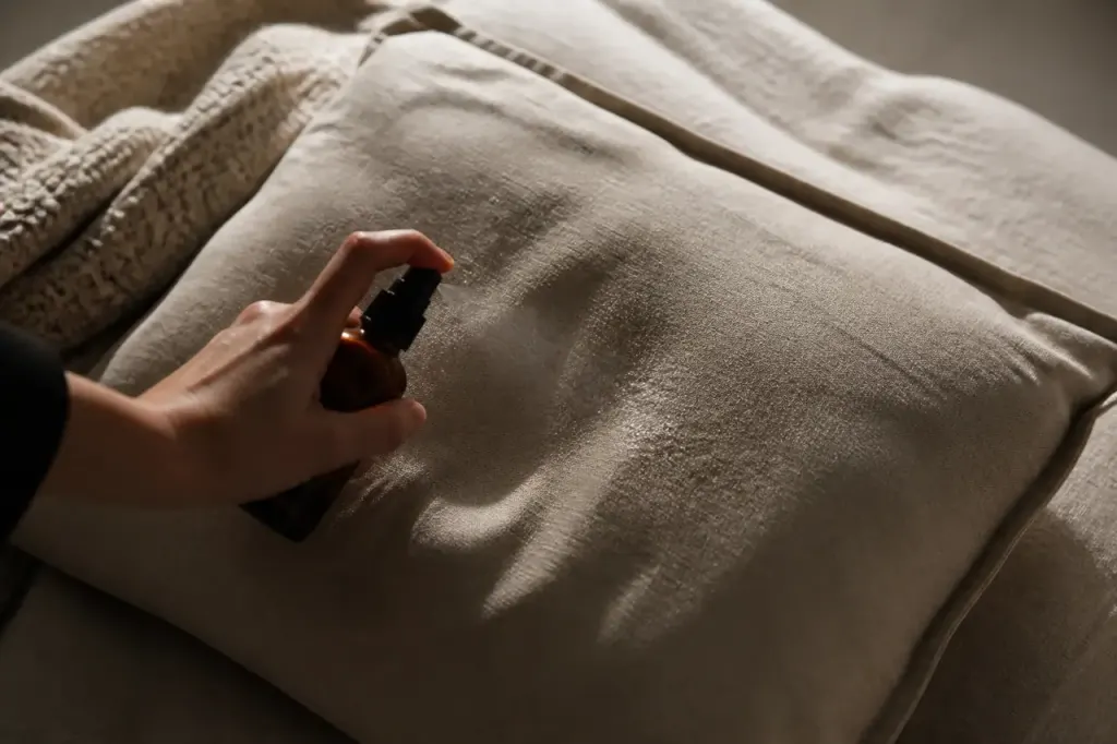 Main tenant un flacon, fines gouttelettes sur coussin beige