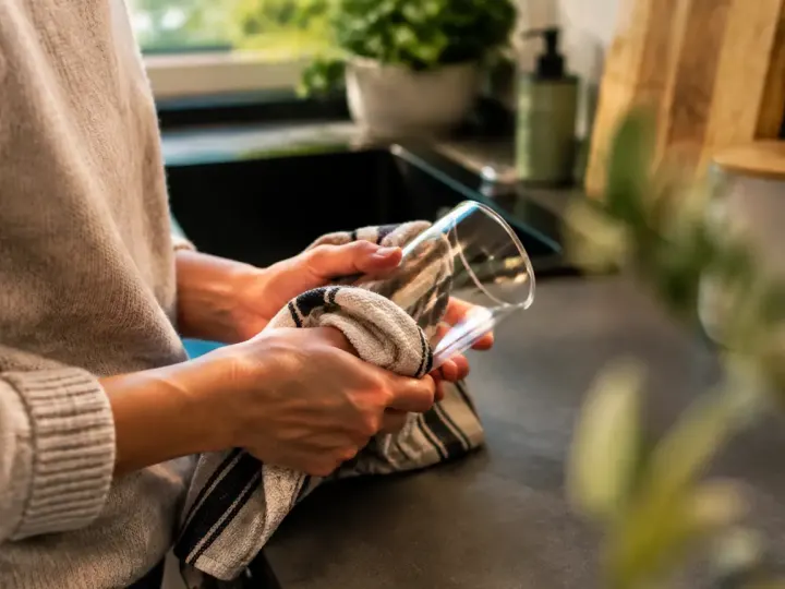 Main essuyant un gobelet transparent sur comptoir cuisine