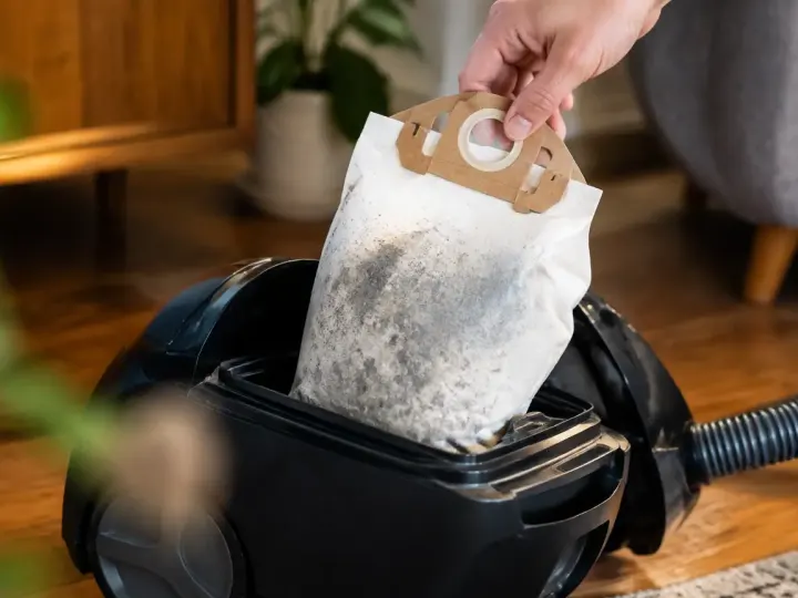Main gantee retirant un sac poussiere plein