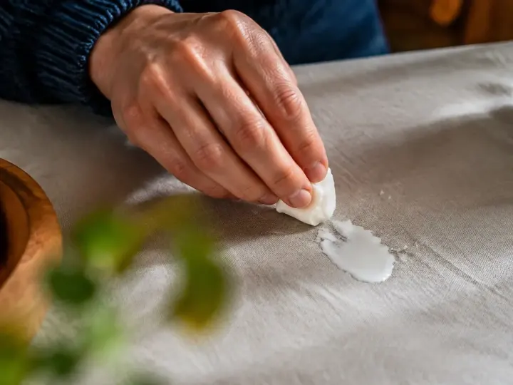 Main grattant une goutte de cire blanche sur nappe
