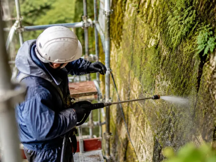 Ouvrier sur echafaudage face a mur couvert de mousse
