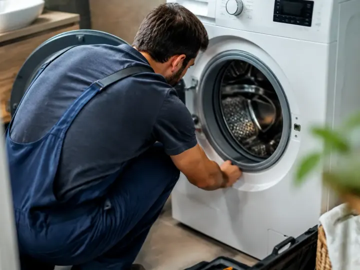 Technicien accroupi devant une machine a laver ouverte